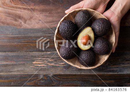 Ripe hass avocado fruit in a basket holding by hand on wooden background 84163576