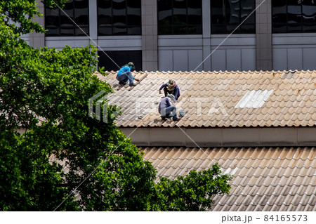 Three handyman workers repairing tiles on the damaged factory roof. 84165573