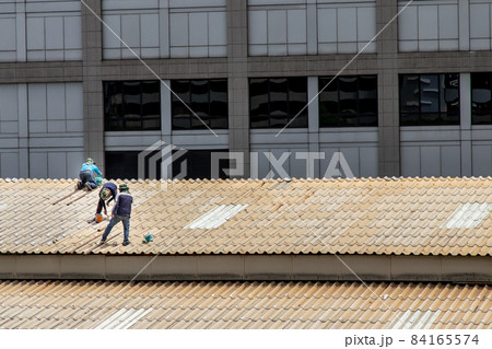 Three handyman workers repairing tiles on the damaged factory roof. 84165574