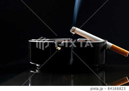 Burning cigarette in a black ash tray Burning cigarette in a black ash tray 84168823