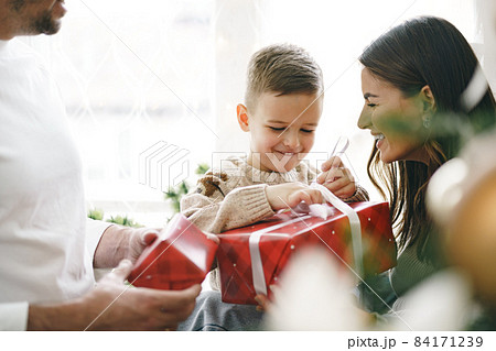 Smiling parents giving Christmas present to son at home Smiling parents giving Christmas present to son at home 84171239