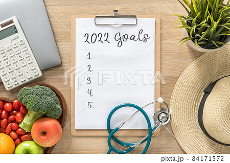 2022 goals on clipboard note pad for new year reminder list of yearly planner, health plan for work-life balance on desk with background of computer, calculator, travel hat and healthy food 84171572