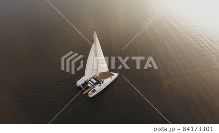 A small sailing yacht sails on the river at sunset A small sailing yacht sails on the river at sunset 84173301