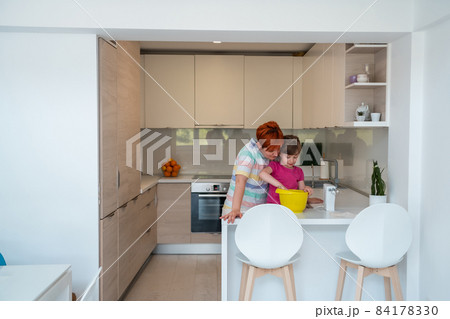 Funny little girl helper playing with dough on his hands learning to knead helps adult mom in the kitchen, happy cute baby daughter and parent mom have fun cooking cookies. Funny little girl helper playing with dough on his hands learning to knead helps adult mom in the kitchen, happy cute baby daughter and parent mom have fun cooking cookies. 84178330