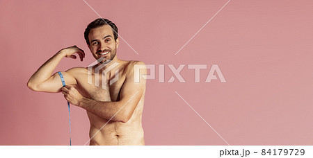 Flyer with young muscular handsome bearded shirtless man measuring his biceps isolated on pink studio background. 84179729