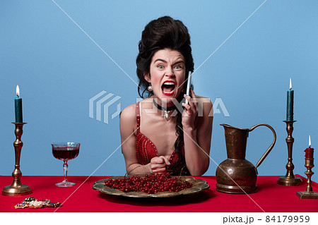 Portrait of young adorable gorgeous woman in dark red, wine color evening dress talking on phone isolated on blue background. 84179959