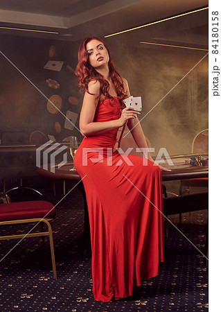 Charnimg sexy woman is posing against a poker table in luxury casino. 84180158