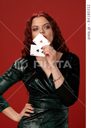 Young sexy woman with a red curly hair holding aces, on a red background. Poker 84180352