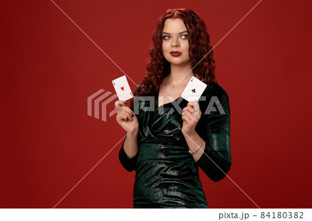 Young sexy woman with a red curly hair holding aces, on a red background. Poker 84180382