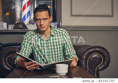 Handsome young man in a barbershop is waiting for the master in the waiting room while drinking coffee 84181797
