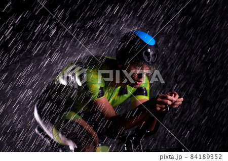triathlon athlete riding bike fast on rainy night 84189352