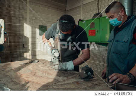 Industrial work during a pandemic. Two men work in a heavy metal factory, wearing a mask on their face due to a coronavirus pandemic 84189755