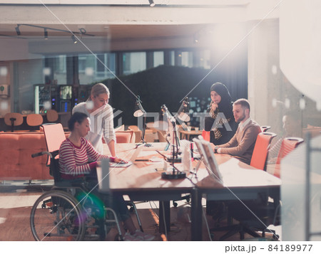Disabled businesswoman in a wheelchair in modern coworking office space. Colleagues in background. Disability and handicap concept. Selective focus 84189977