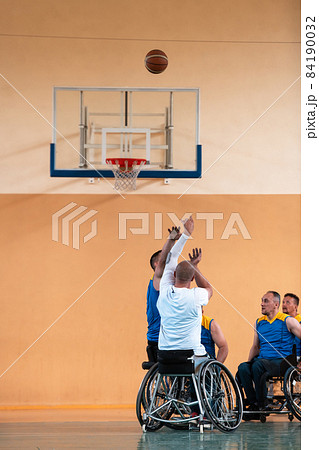 Disabled War veterans mixed race and age basketball teams in wheelchairs playing a training match in a sports gym hall. Handicapped people rehabilitation and inclusion concept 84190032