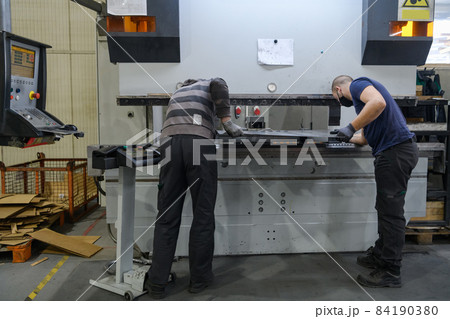two workers wearing a protective mask due to a coronavirus pandemic, working in a modern factory and preparing a program and materials for a cnc machine 84190380