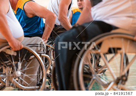Close up photo of wheelchairs and handicapped war veterans playing basketball on the court 84191567