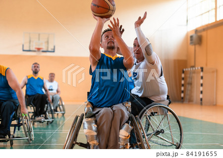 Disabled War veterans mixed race and age basketball teams in wheelchairs playing a training match in a sports gym hall. Handicapped people rehabilitation and inclusion concept Disabled War veterans mixed race and age basketball teams in wheelchairs playing a training match in a sports gym hall. Handicapped people rehabilitation and inclusion concept 84191655