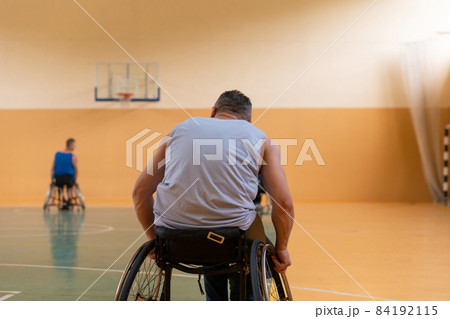 Close up photo of wheelchairs and handicapped war veterans playing basketball on the court 84192115