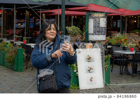 An Asian woman takes a selfie in front of a restaurant. Picture from the market square, Grote Markt, in Bruges, Belgium. An Asian woman takes a selfie in front of a restaurant. Picture from the market square, Grote Markt, in Bruges, Belgium. 84196860