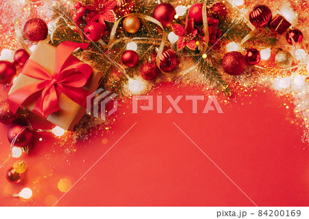 Festive boxes with a satin red bow on a red background with Christmas toys balls, a branch of fluffy fir tree, sparkles with confetti lights. New Year Flat festive mockup with copy space 84200169