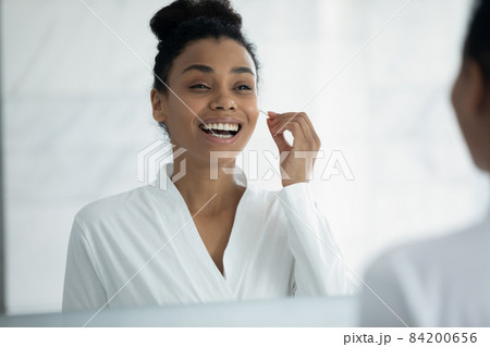 Happy young african american woman cleaning ears with cotton swab. Happy young african american woman cleaning ears with cotton swab. 84200656