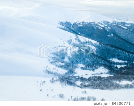 Aerial shot of majestic sunrise in the mountains. Valley between the mountains is covered with fog and is illuminated by the warm rays of the rising sun. Mountains covered with forest natural. 84200771