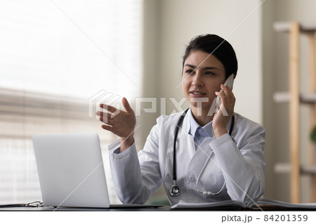 Smiling Indian woman doctor talking on phone, consulting patient Smiling Indian woman doctor talking on phone, consulting patient 84201359