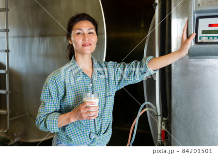Asian woman dairy farm worker standing with glass of milk Asian woman dairy farm worker standing with glass of milk 84201501