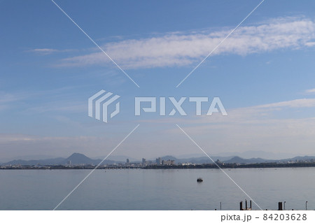 琵琶湖と対岸の橋と樹々の森と街と山と雲と青空のある風景 84203628