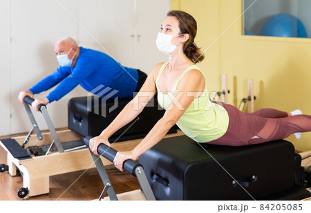 Young woman in protective mask doing pilates exercises on reformer Young woman in protective mask doing pilates exercises on reformer 84205085