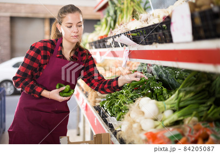 Focused young saleswoman puts pepper on the counter Focused young saleswoman puts pepper on the counter 84205087