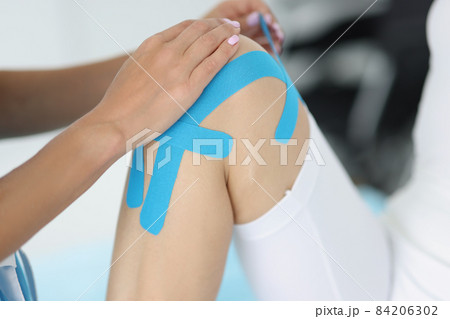 Physiotherapist apply kinesiology tape to patient knee in clinic Physiotherapist apply kinesiology tape to patient knee in clinic 84206302