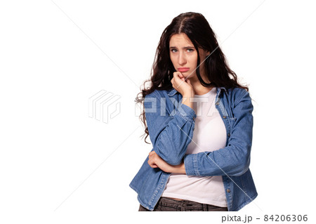 Beautiful and unhappy young woman with dark wavy hair looking into the camera with serious expression on her face. 84206306