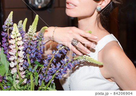 Woman hands with manicure and luxury jewelry rings. Close up of female hand on flowers showing fashion jewelry at camera. Concept of manicure and fashion. 84206904