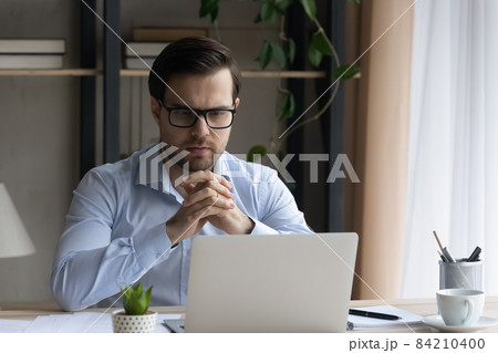 Pensive young businessman in glasses working on computer. Pensive young businessman in glasses working on computer. 84210400