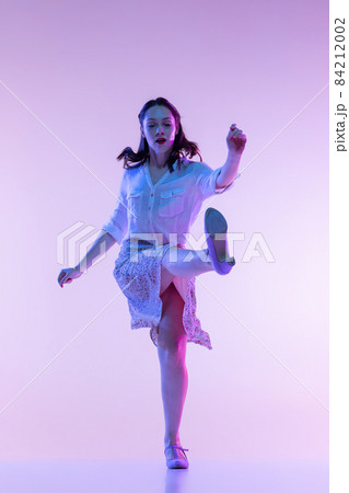 Portrait of young excited woman in vintage retro style clothes dancing isolated on lilac color background in neon light Portrait of young excited woman in vintage retro style clothes dancing isolated on lilac color background in neon light 84212002