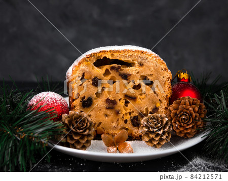 Christmas fruitcake powdered sugar on white plate dark background seasonal decorations. Xmas atmospheric greeting card. 84212571