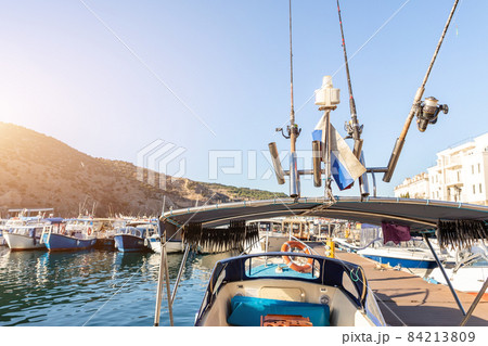 Close-up detail of many fishing rods and drying catch fish under roof of small ship moored fisherman village marina bay on bright sunny day. Sea harbor with traditional retro vessels background 84213809
