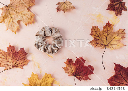 Brown velvet scrunchie and autumn red and yellow maple leaves backround. Trendy accessories from 80s and 90s. Flatlay, top view. Hairstyle, outfit ideas for fall concept 84214548