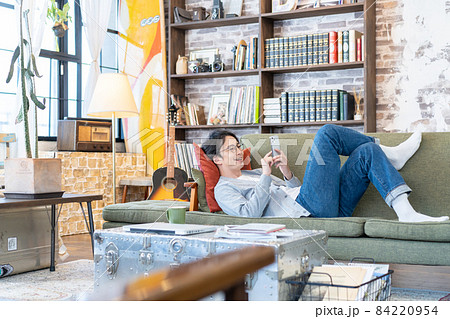 リビングのソファでスマホを見ながら笑う若い男性 リビングのソファでスマホを見ながら笑う若い男性 84220954