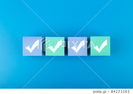 Four white checkmarks on multicolored cubes in a row against blue background  84221163