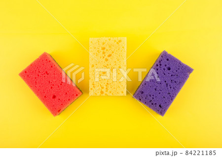 Close up of three multicolored red, purple and yellow cleaning sponges on bright yellow background 84221185