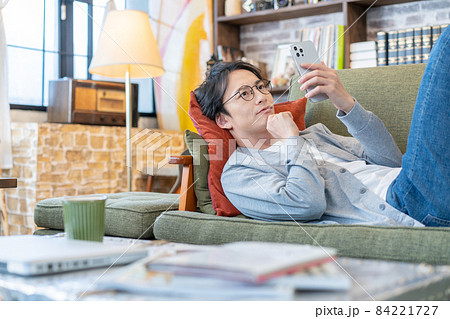 リビングのソファでスマホでテレビ電話をしながら笑う若い男性 リビングのソファでスマホでテレビ電話をしながら笑う若い男性 84221727