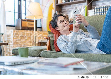 リビングのソファでスマホでテレビ電話をしながら笑う若い男性 リビングのソファでスマホでテレビ電話をしながら笑う若い男性 84221728
