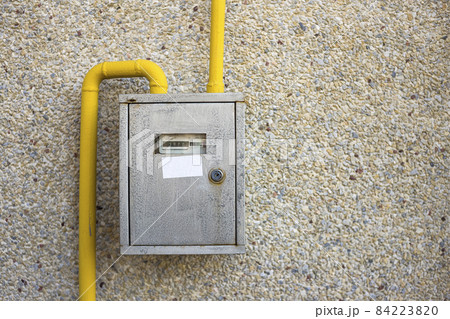 Close-up of metal steel gas meter box with connecting yellow pipes hanging on exterior light stone house wall. Construction, renovation, measurement tool and energy saving concept. Close-up of metal steel gas meter box with connecting yellow pipes hanging on exterior light stone house wall. Construction, renovation, measurement tool and energy saving concept. 84223820
