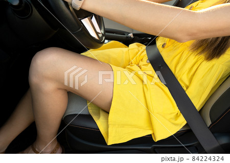 Young woman driver legs in yellow summer dress behind steering wheel driving a car. Young woman driver legs in yellow summer dress behind steering wheel driving a car. 84224324