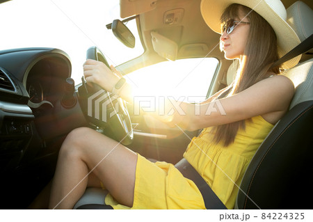 Young woman driver in summer yellow dress and straw hat driving a car. 84224325