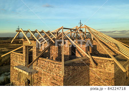 Private residential house with wooden roof frame structure under construction. Unfinished brick building under development. Private residential house with wooden roof frame structure under construction. Unfinished brick building under development. 84224718