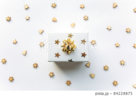 Gift white box with a gold ribbon with tinsel and wooden Christmas confetti on a white background. Gift concept, new year, festive background Gift white box with a gold ribbon with tinsel and wooden Christmas confetti on a white background. Gift concept, new year, festive background 84229875