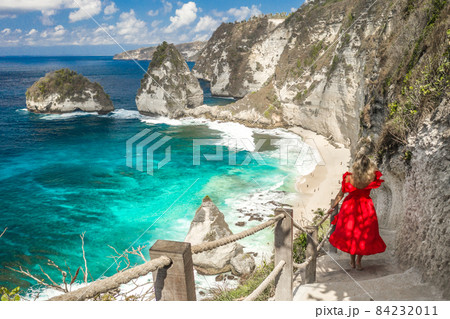 Back view woman wearing a red dress on standing on the stairs leading down at Diamond beach in Nusa 84232011
